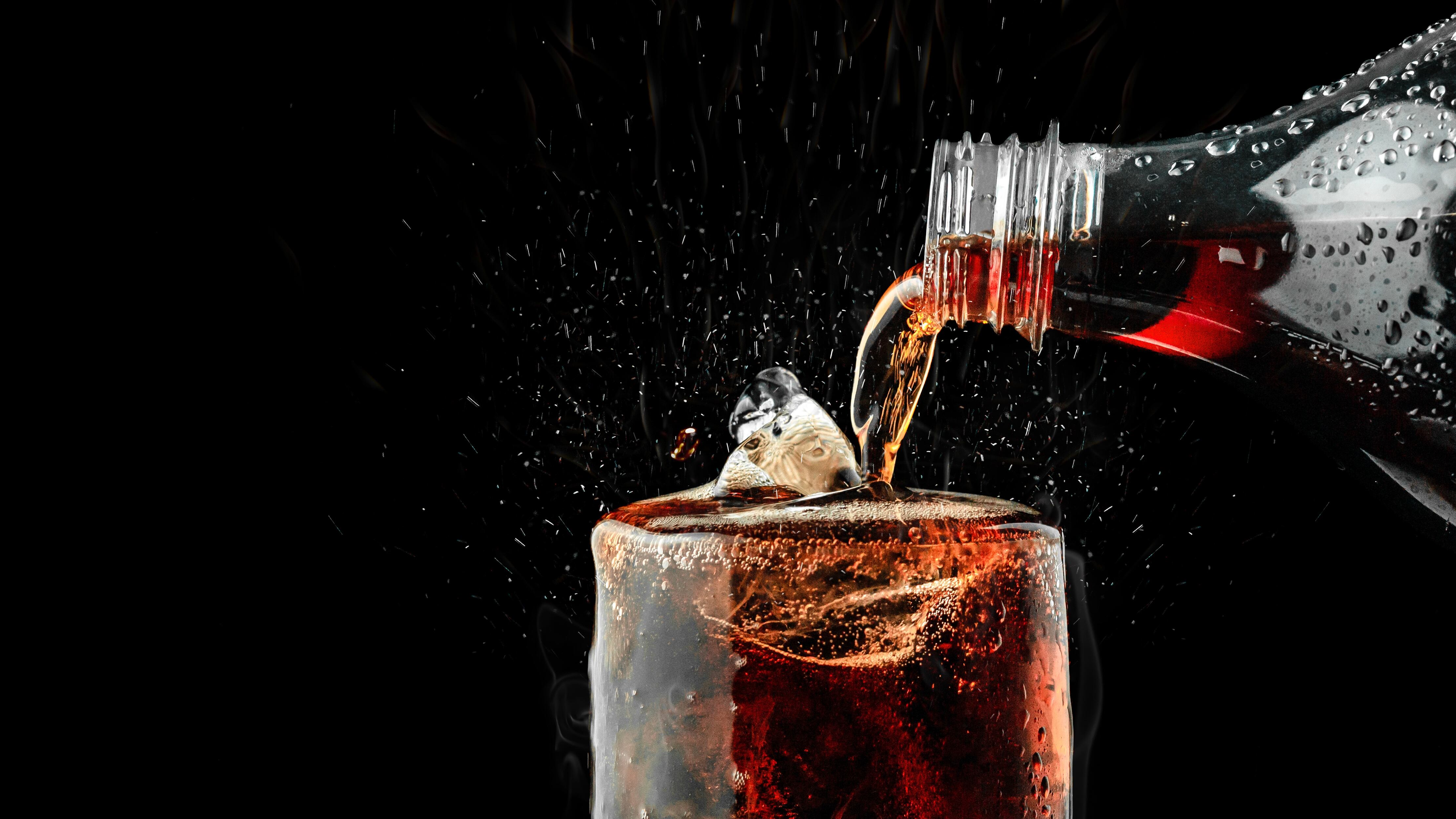 Pour soft drink in glass with ice splash on dark background.