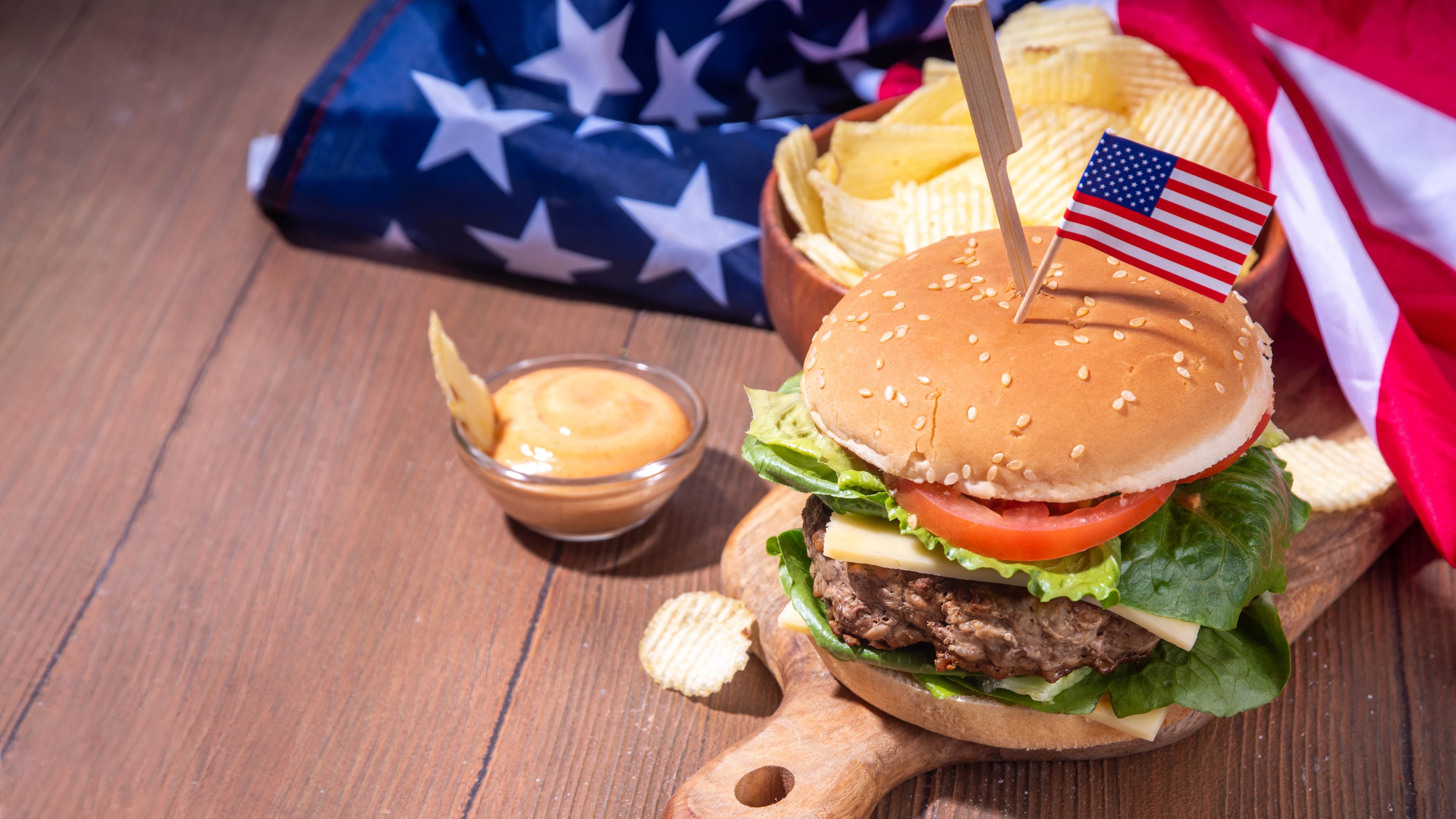 Tasty cheeseburger, chips and sauce with patriotic American flag.