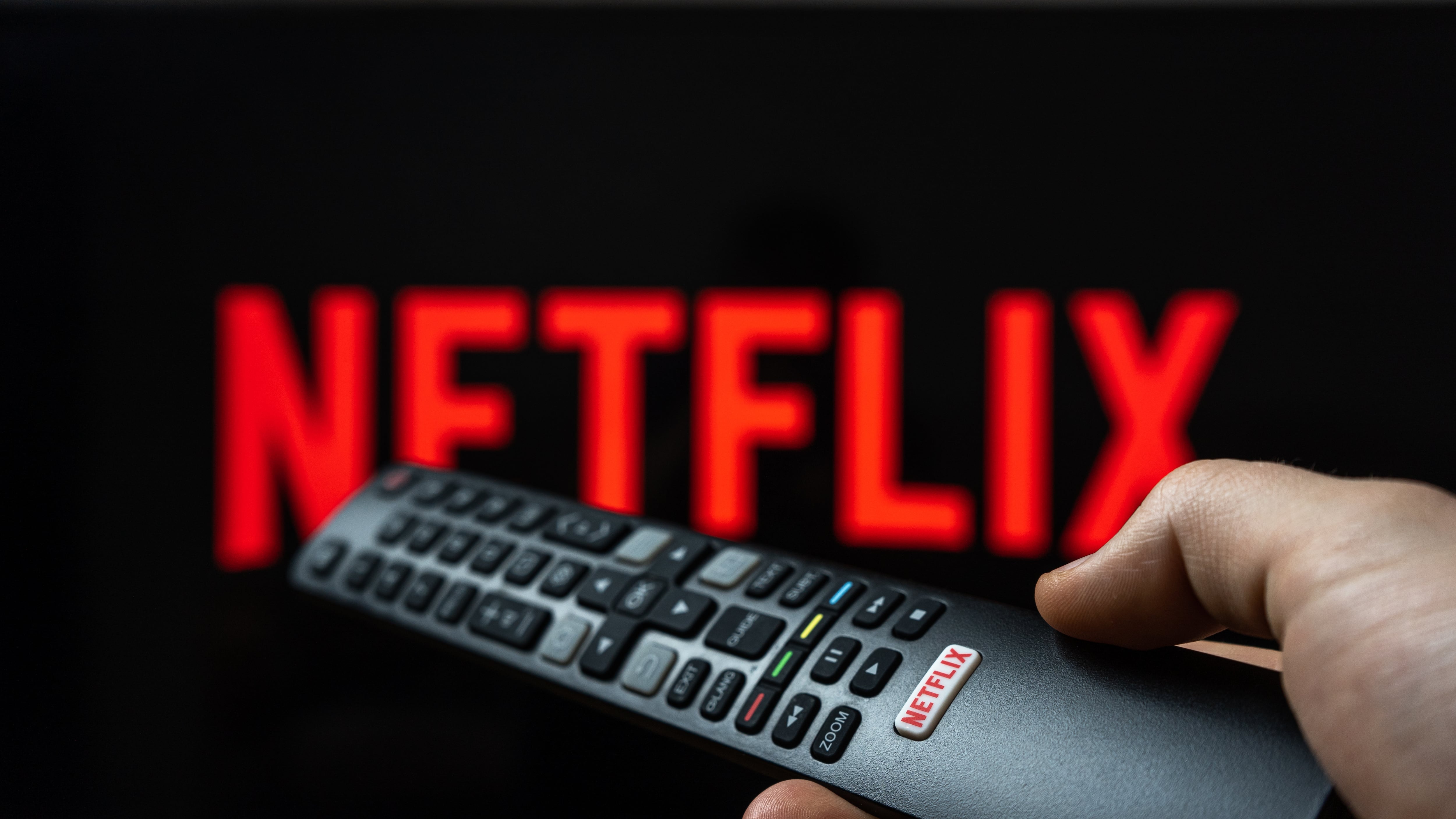 Holding TV remote controller with Netflix logo. Turning on Netflix platform on TV