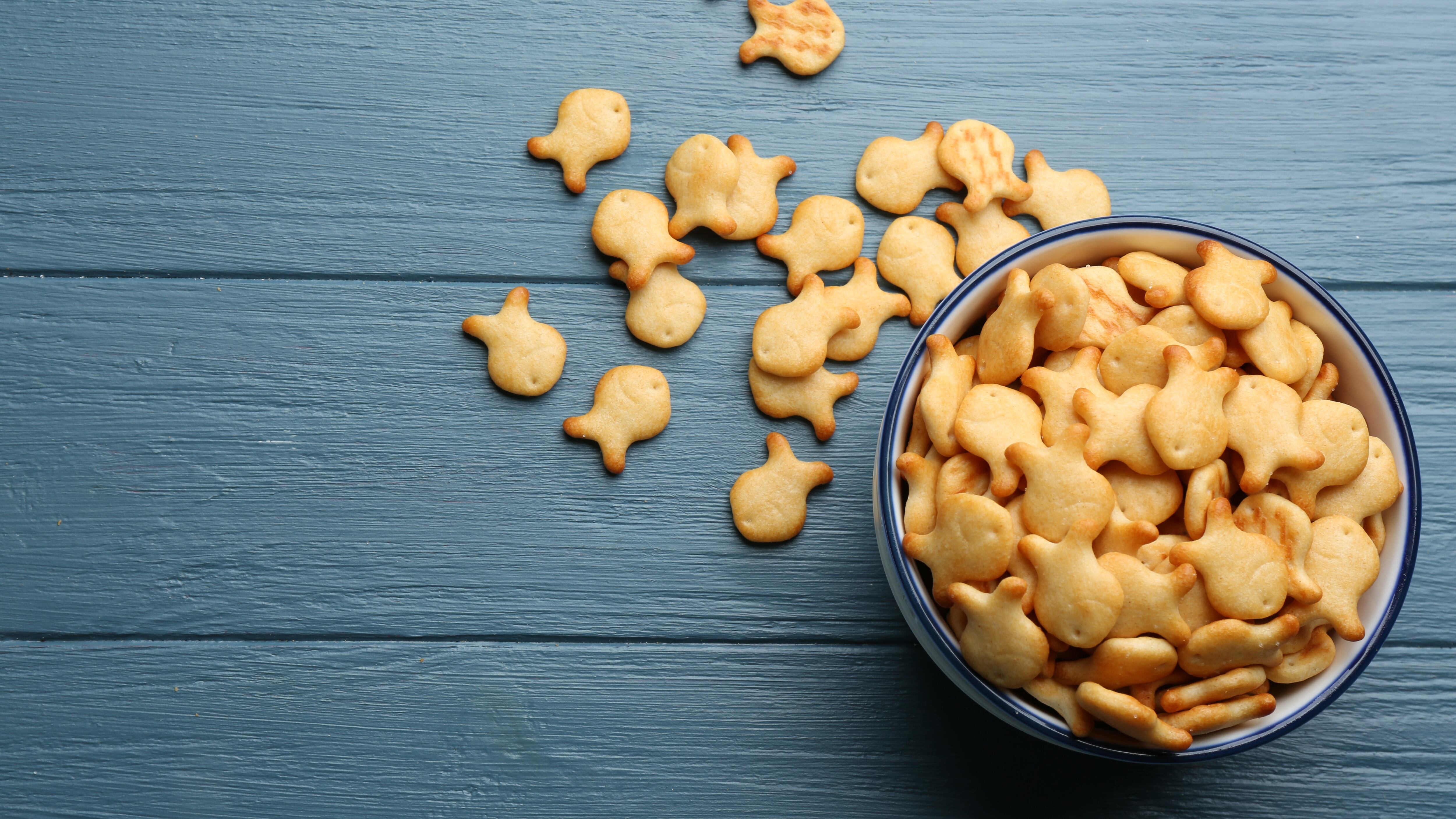 Goldfish crackers in bowl on blue wooden table, flat lay