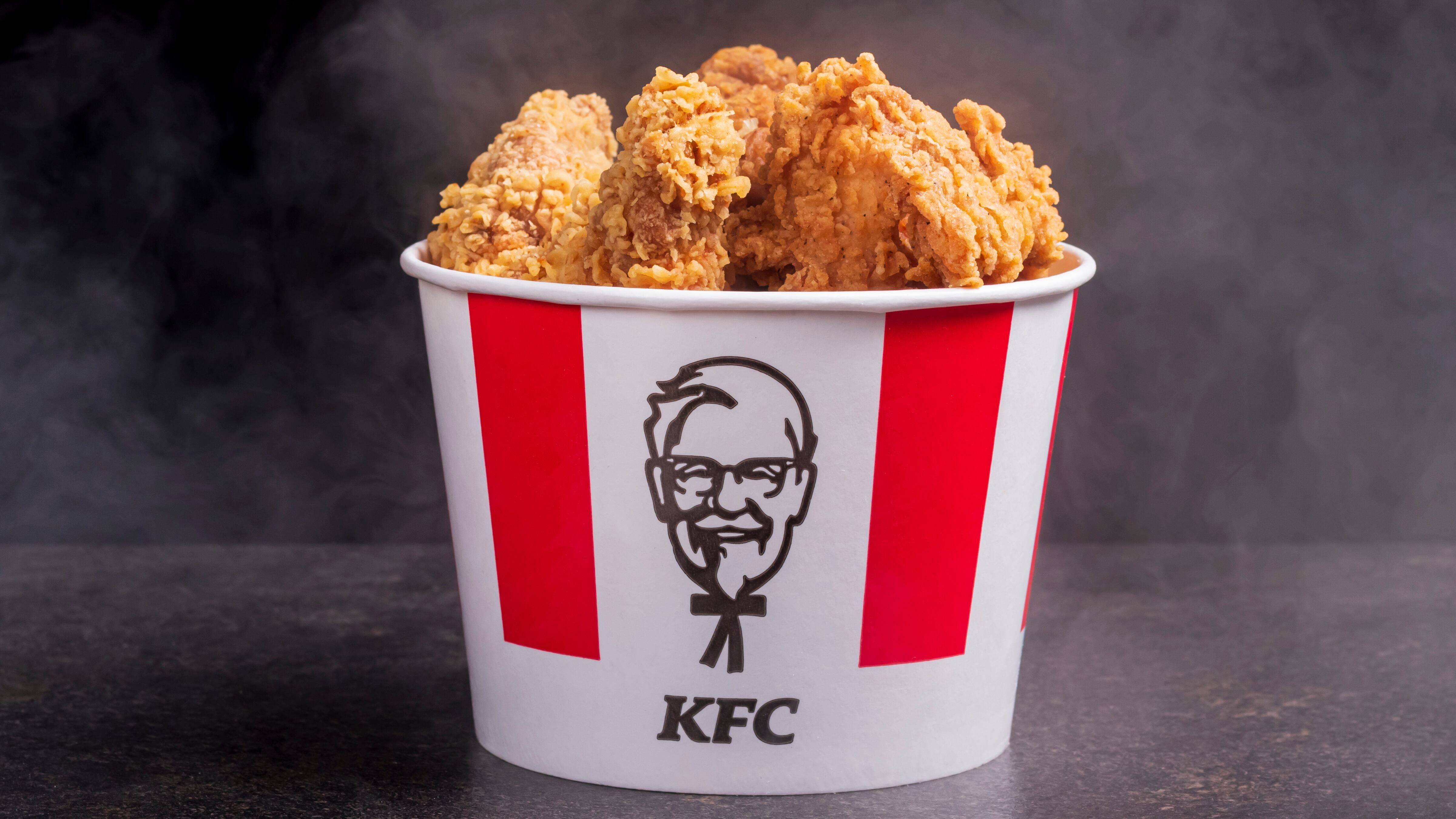 black background, night. Lots of hot wings or strips of KFC chicken in a KFC Kentucky Fried Chicken fast food bucket